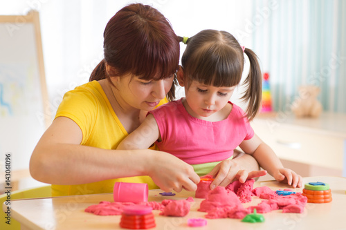 Cute kid and mother playing with sculpting toy at home. Little girl building sandcastle.