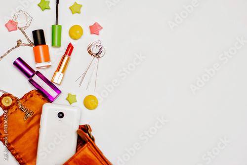Fashion concept : Flat lay of orange leather woman bag open out with cosmetics, accessories and smartphone on white background