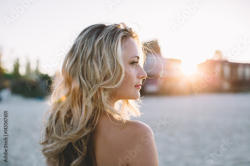 Beautiful young blonde in black dress walking along the seashore and posing at sunrise in summer