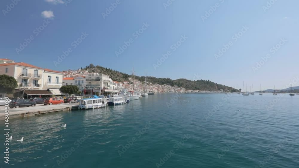 Sail near the Greek island. Sailboat sails behind the seafront of Poros. Sail near the Greek island. Sailboat sails behind the seafront of Poros.