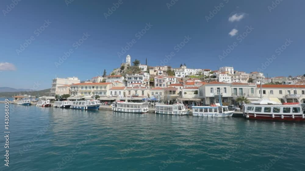 Sailboat sails behind the seafront of island. Sail near Greek island Poros. Sailboat sails behind the seafront of island. Sail near Greek island Poros.