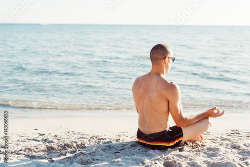 Young man doing yoga on the beach - meditation, relaxing, zen concept