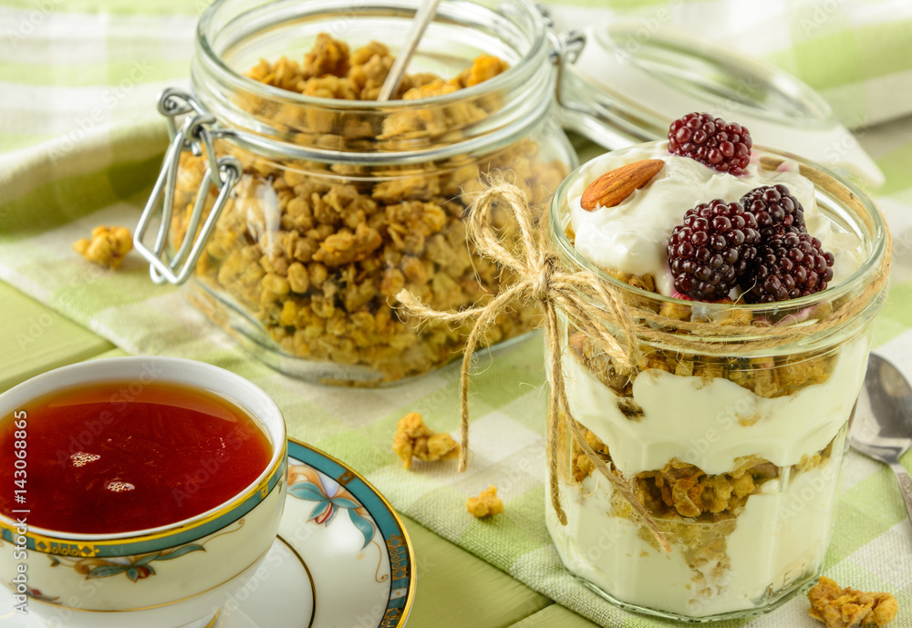 Healthy breakfast ingredients. Homemade granola with yogurt in open glass jar and cup of tea. The food is rich in useful carbohydrates, vitamins and nutrients that are essential for health. Healthy breakfast ingredients. Homemade granola with yogurt in open glass jar and cup of tea. The food is rich in useful carbohydrates, vitamins and nutrients that are essential for health.