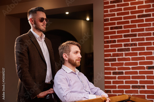 Photo of young handsome man who sitting in chair at barbershop with hairdresses who standing by the armchair photo