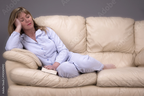 Woman wearing blue and white striped pyjamas sleeping on a cream leather settee