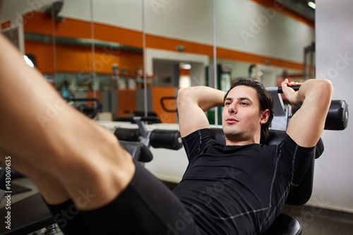 Athletic man in the black sportwear doing exercises on legs in gym.