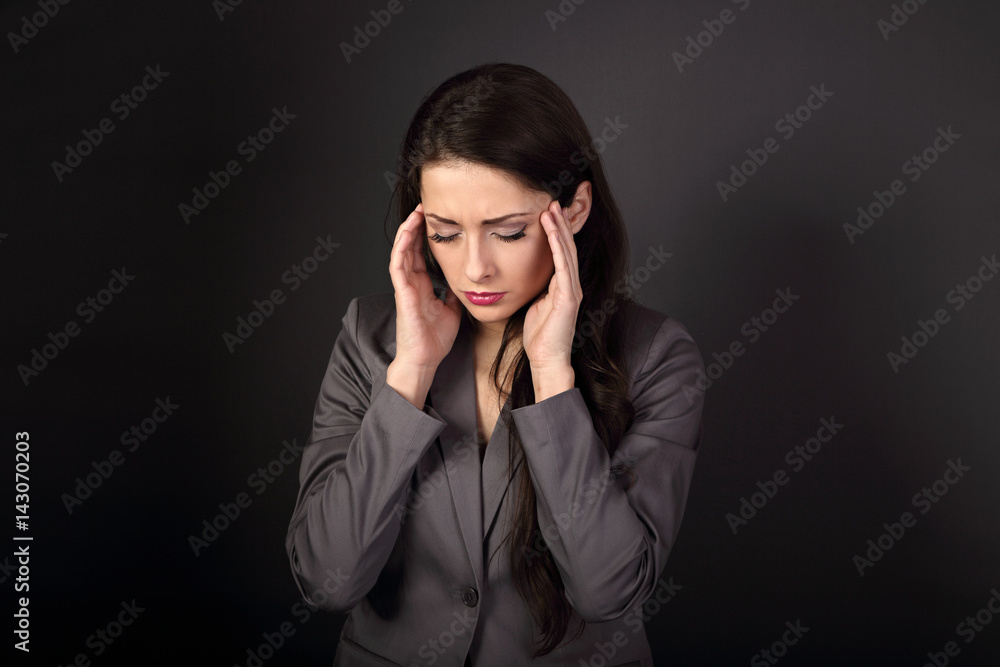 Unhappy stressed migraine business woman with closed eyes in suit holding head the hands on dark grey background Unhappy stressed migraine business woman with closed eyes in suit holding head the hands on dark grey background