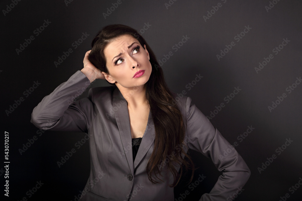 Serious unhappy business woman in suit looking up and thinking on dark grey background with empty copy space Serious unhappy business woman in suit looking up and thinking on dark grey background with empty copy space