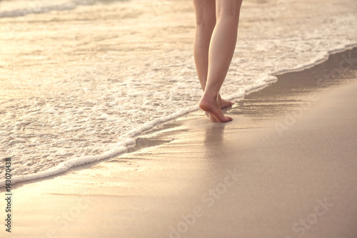 Closeup of a woman bare feet walking at a beach at sunset  with a wave foaming - travel and relaxing  copy space