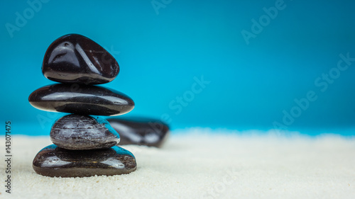 Growing piled up of four black pebbles on bright sand with blue background