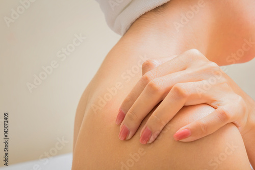 Young woman sitting on the bed suffering from pain in shoulder