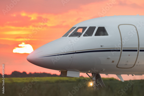 Nose of a private business jet on the runway with the sun in the background