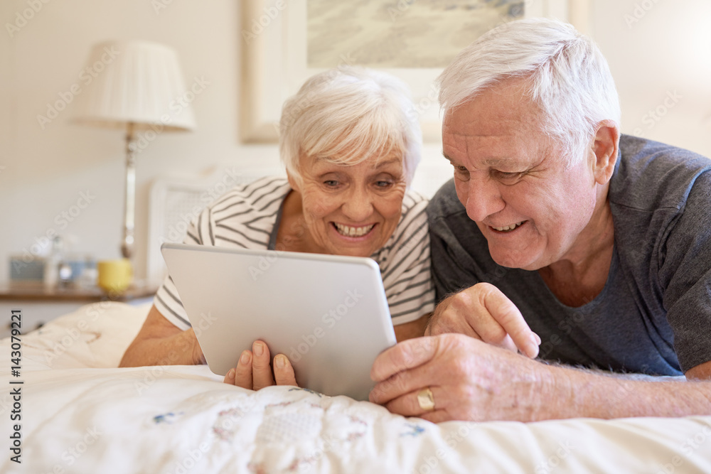 Smiling senior couple using a digital tablet together in bed Smiling senior couple using a digital tablet together in bed