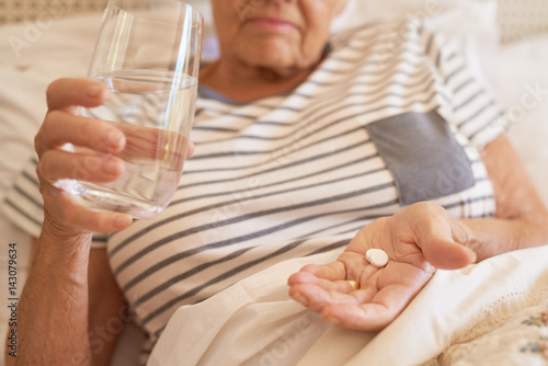 Senior woman lying in bed taking medicine in the morning