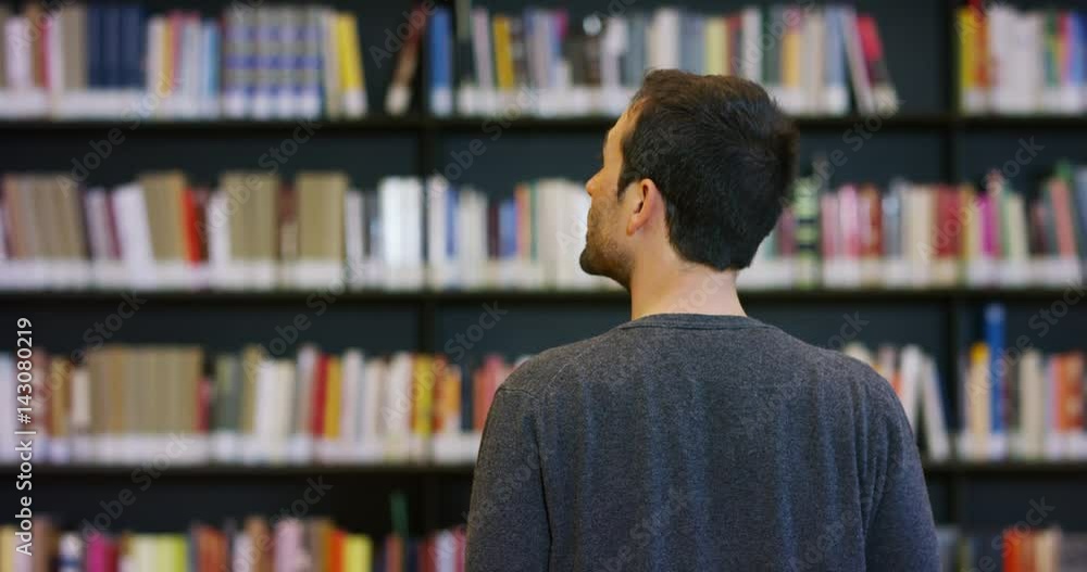 Portrait of a beautiful young man smiling happy in a library holding books after doing a search and after studying. Concept: educational, portrait, library, and studious. Portrait of a beautiful young man smiling happy in a library holding books after doing a search and after studying. Concept: educational, portrait, library, and studious.
