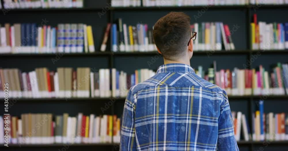 Portrait of a beautiful young man smiling happy in a library holding books after doing a search and after studying. Concept: educational, portrait, library, and studious. Portrait of a beautiful young man smiling happy in a library holding books after doing a search and after studying. Concept: educational, portrait, library, and studious.