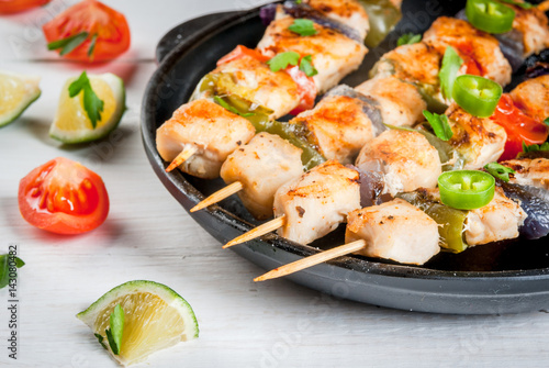 Fajita chicken kebabs, with chicken meat, pepper, chili, tomatoes, onions, lime juice and herbs. In a frying pan, on a white wooden table. Mexican cuisine, a traditional food,