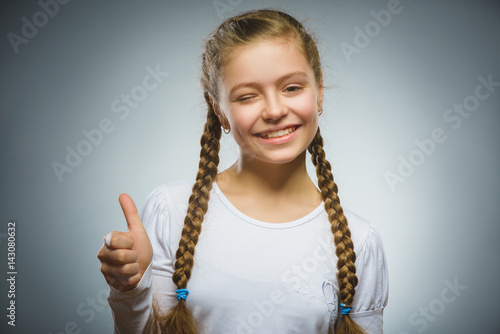 Happy girl showing thubs up. Closeup Portrait child smiling isolated on grey