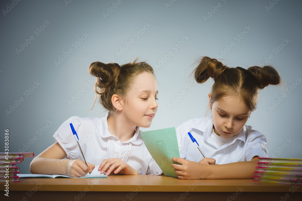 Happy girls sitting at desk on gray background. school concept Happy girls sitting at desk on gray background. school concept