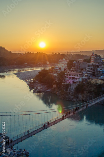 View of River Ganga and Lakshman Jhula bridge at sunset with a blue sky and colorful houses. Rishikesh. India. HDR image