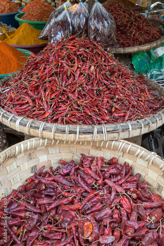 A lot of dried chilies in woven baskets and heaps of different spices at the Zegyo (also known as Zay Cho) Market in Mandalay, Myanmar (Burma).