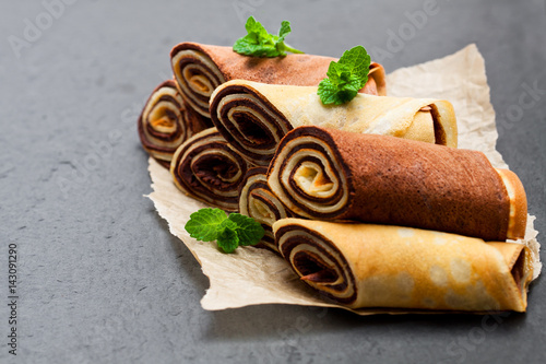 Rolled  milk and chocolate pancakes on black stone background