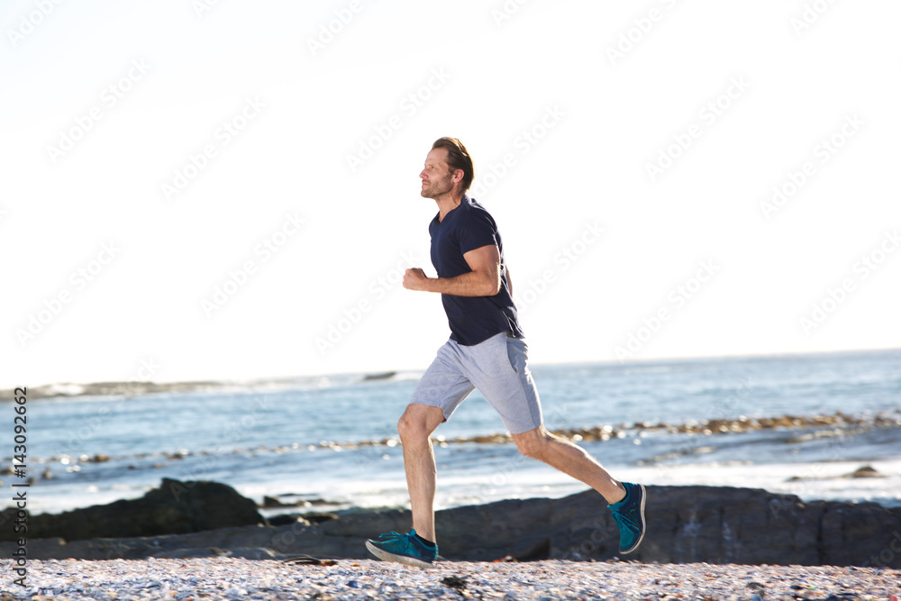 full body portrait of active man running by beach