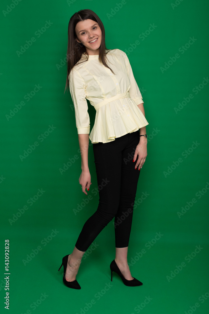 Beautiful brunette in a yellow blouse and black pants on a green background Beautiful brunette in a yellow blouse and black pants on a green background