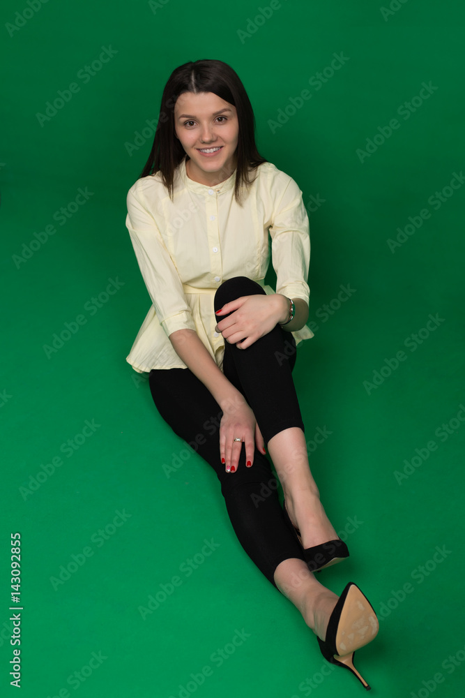 Beautiful brunette in a yellow blouse and black pants on a green background Beautiful brunette in a yellow blouse and black pants on a green background