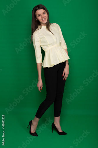 Beautiful brunette in a yellow blouse and black pants on a green background