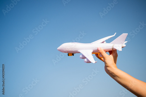 white toy plane in female hand on sunny blue sky