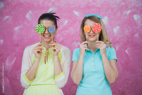 Two beautiful young women hides eyes with sweet lollipops.