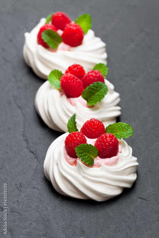 Mini Pavlova meringue nests with raspberries and mint on black stone background Mini Pavlova meringue nests with raspberries and mint on black stone background