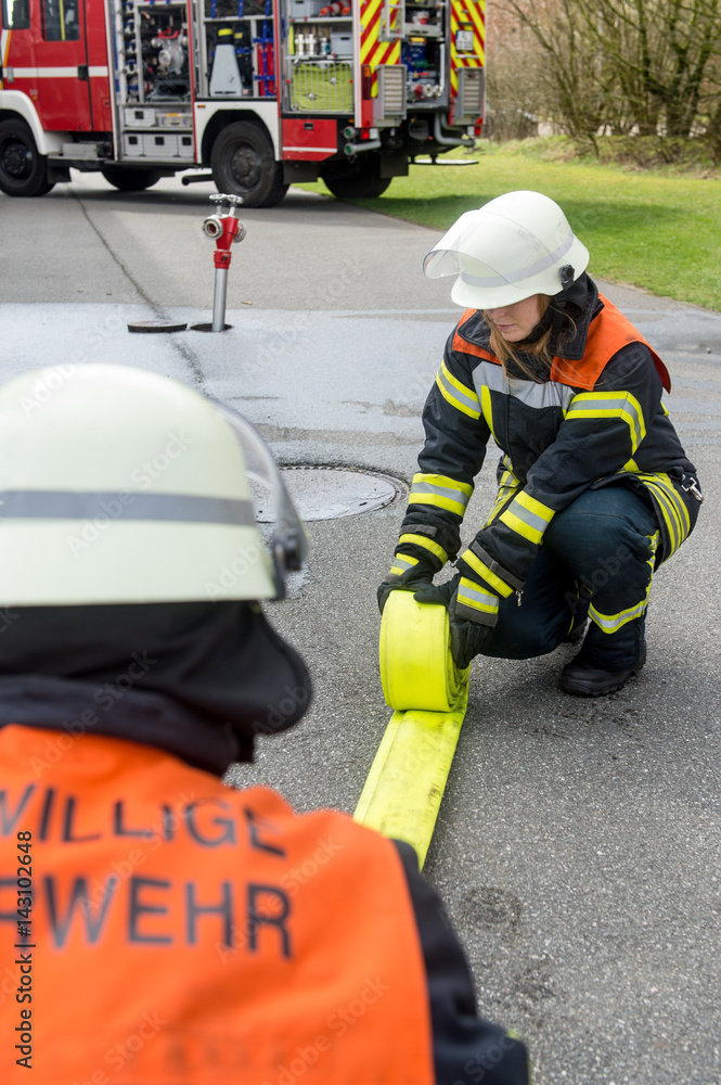 Naklejka premium Feuerwehrmänner rollen einen Feuerwehrschlauch ein