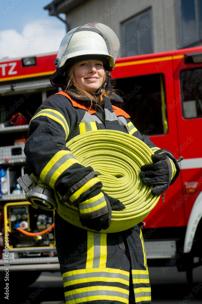 Fototapeta premium Junge Feuerwehrfrau trägt einen Schlauch