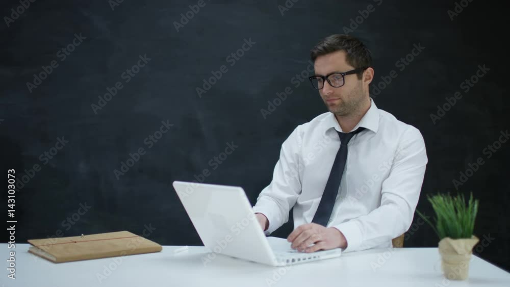 Portrait smiling businessman using laptop on blank chalkboard background Portrait smiling businessman using laptop on blank chalkboard background