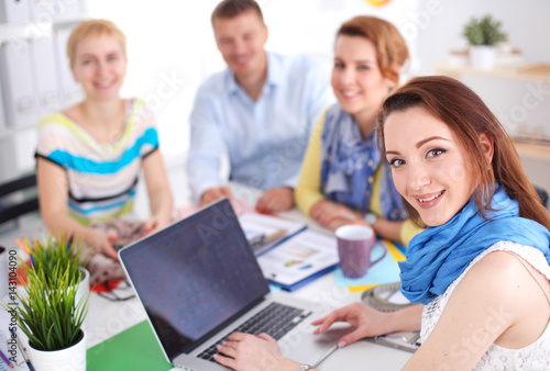 Portrait of attractive female designer sitting on desk in office