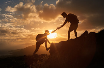 Male and female hikers climbing up mountain cliff and one of them giving helping hand. People helping and, team work concept.


