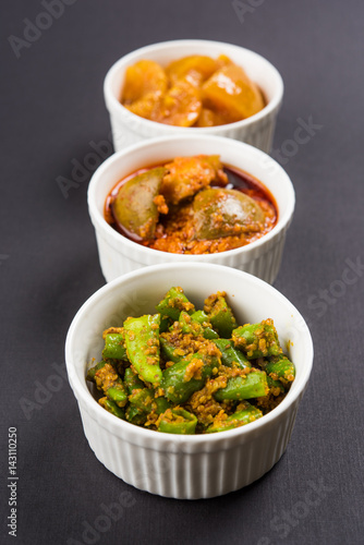 Group photograph of indian pickles like mango pickle , lemon pickle and green chilli pickle, sarved in ceramic bowls, selective focus photo