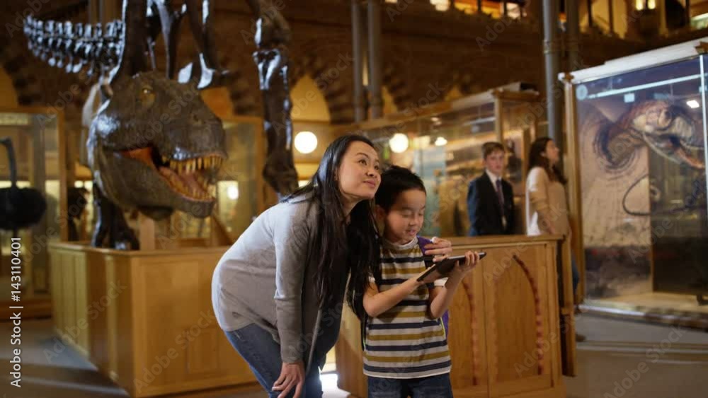 Mother & son in museum, standing by dinosaur skeleton & looking at computer Mother & son in museum, standing by dinosaur skeleton & looking at computer
