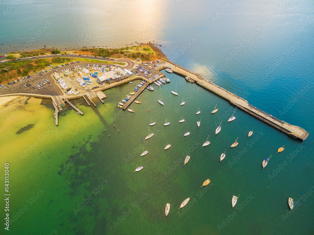 Aerial drone view of Mornington Pier and Yacht club with moored boats nearby. Vivid turquoise bay water. Melbourne, Victoria, Australia
