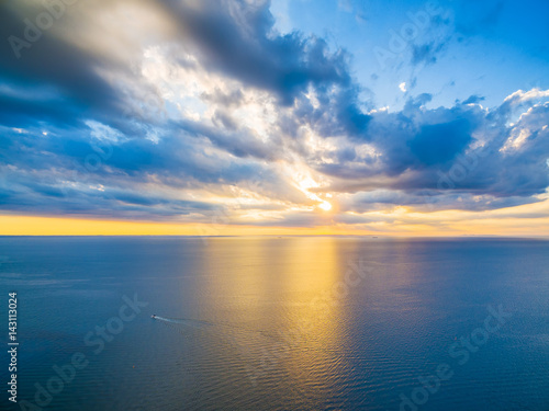Aerial panoramic view of lonely boat sailing across ocean at beautiful sunset. Beautiful glowing yellow light reflecting in blue bay waters