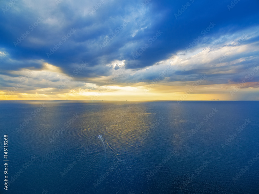 Aerial view of lonely boat sailing across ocean at beautiful sunset