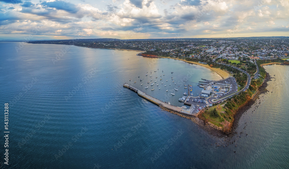 Fototapeta premium Aerial panoramic view of Mornington Pier and Peninsula coastline, showcasing the yacht club, moored boats, and suburban area at sunset. Melbourne, Victoria, Australia