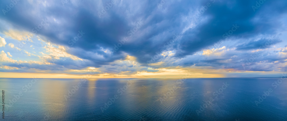 Aerial panoramic view of ocean water and beautiful blue skies at glowing yellow sunset. Nothing but water and clouds