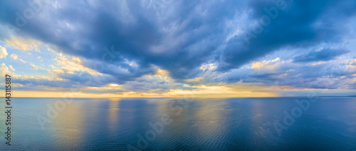 Aerial panoramic view of ocean water and beautiful blue skies at glowing yellow sunset. Nothing but water and clouds © Greg Brave