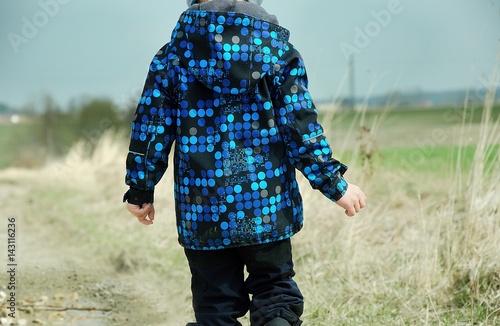 Boy wearing softshell jacket and walking along a dirt road in chilly and windy weather. Child concept.