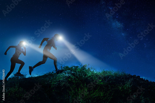 Night trail runner of men and women running on the mountain.at night milky way
