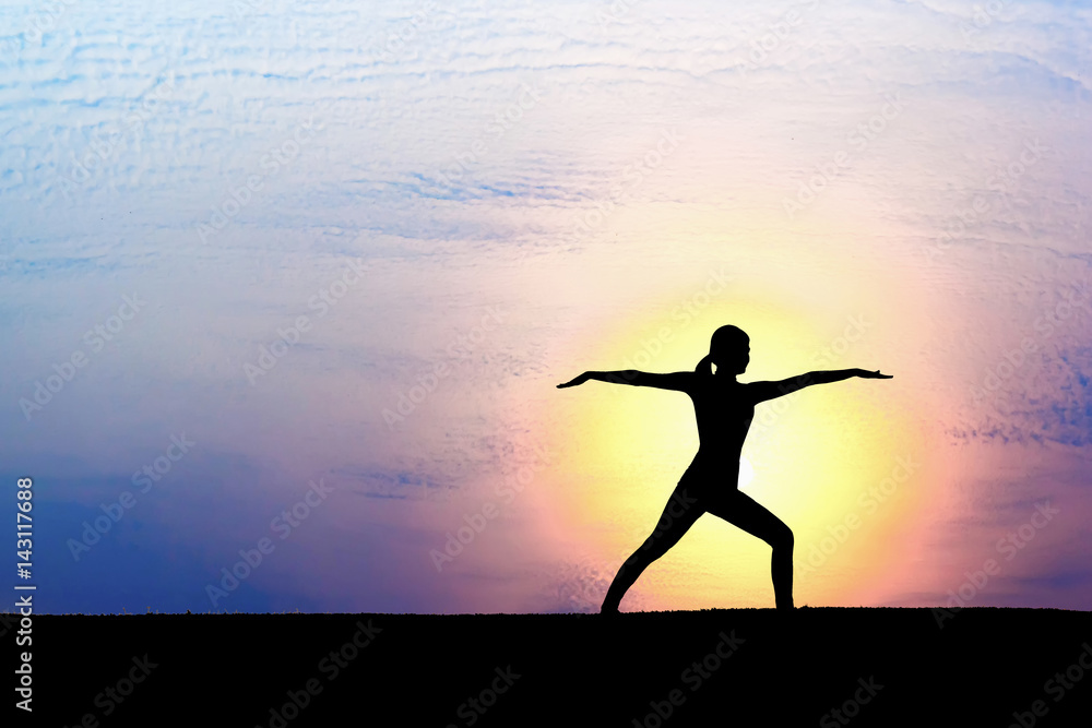 Woman practicing warrior yoga pose outdoors over sunset sky background.