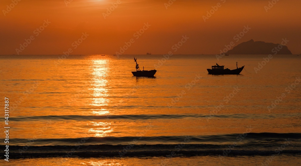 A fiery orange sunrise sky looking out over the south China sea in Vung Lam Bay Vietnam. With fishing boats in silhouette.